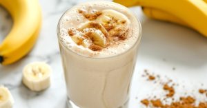 Banana milkshake in a glass topped with slices of banana and cinnamon.