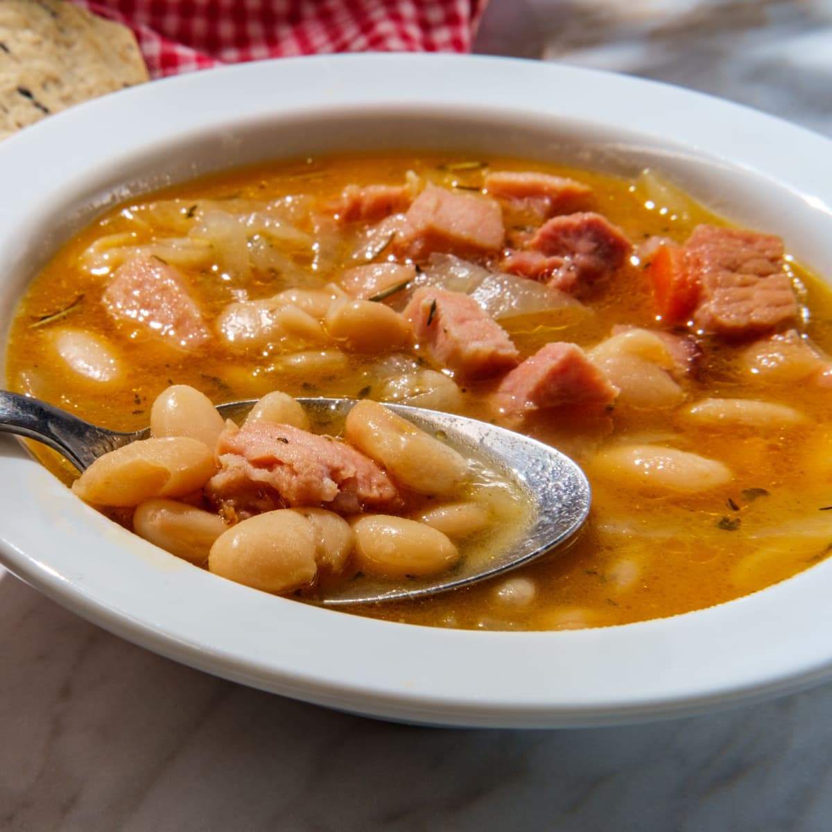 Spoon dipped in a bowl of bean soup with ham. 