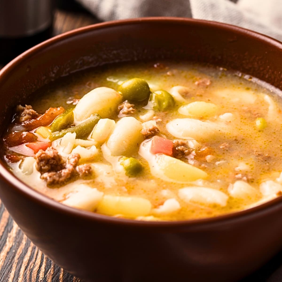 Busy day soup with broth, ground beef, green peas, carrots and macaroni soup on a wooden bowl. 