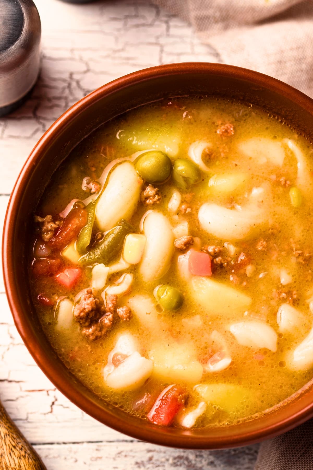 Busy day soup on a wooden bowl with green peas, elbow macaroni, ground meat and carrots. 