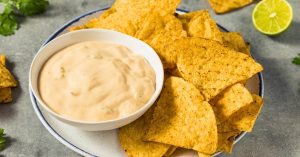 Bowl of queso cheese dip with tortilla on a plate