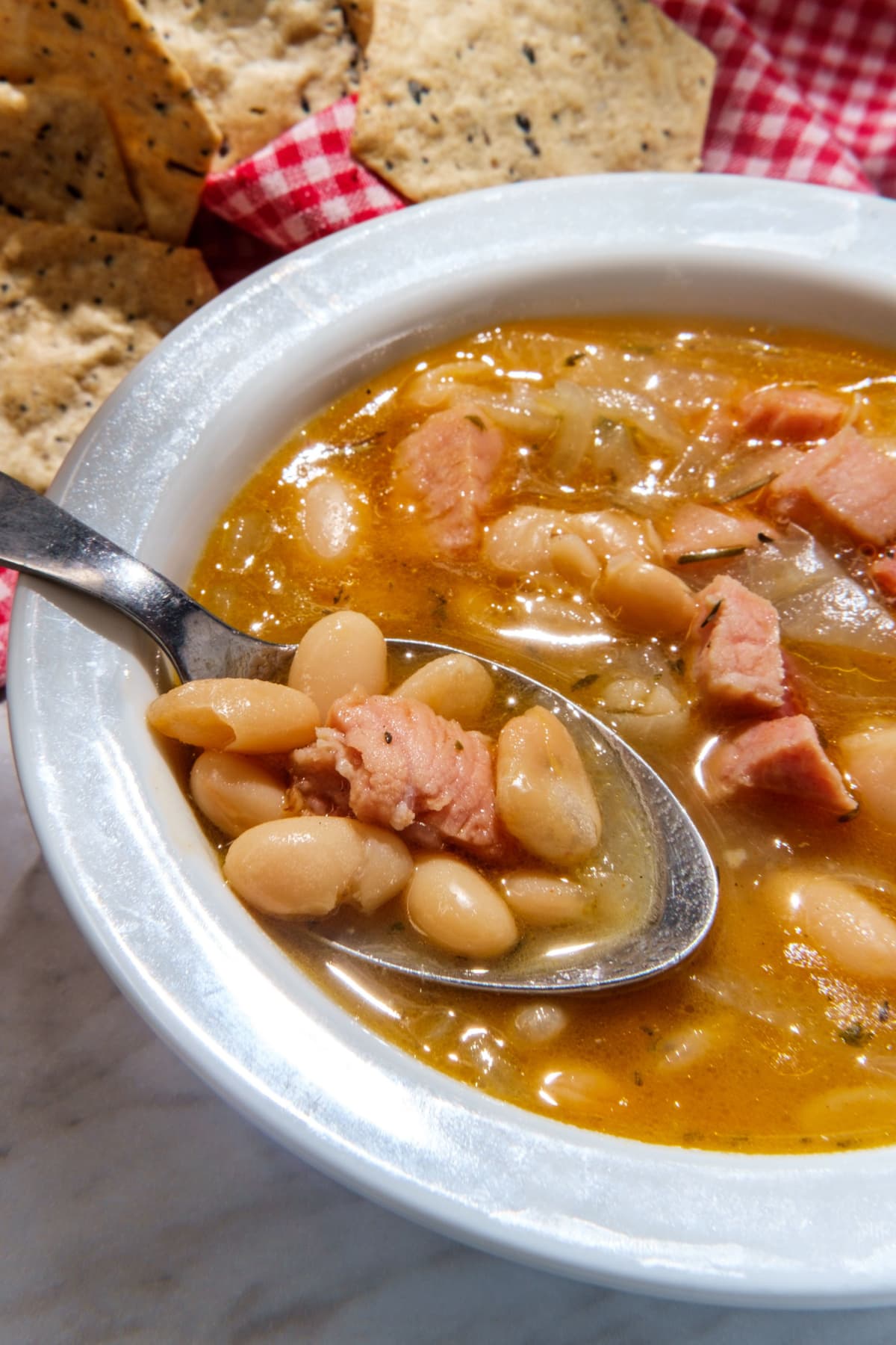 A bowl of bean soup with spoon and bread beside on a table.