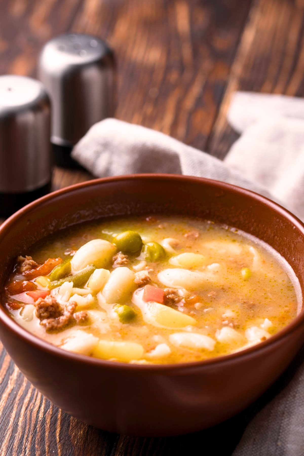 Busy day soup made with elbow macaroni, broth, green peas, carrots and ground meat on a wooden bowl. 