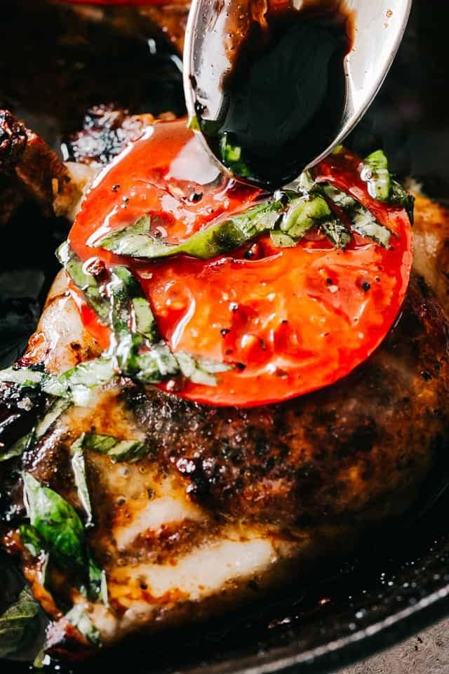 Grilled porkchops garnished with tomato slice and copped parsley drizzled with balsamic vinegar. 