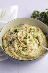 Pasta with creamy sauce and shredded chicken meat served on a bowl with fork.