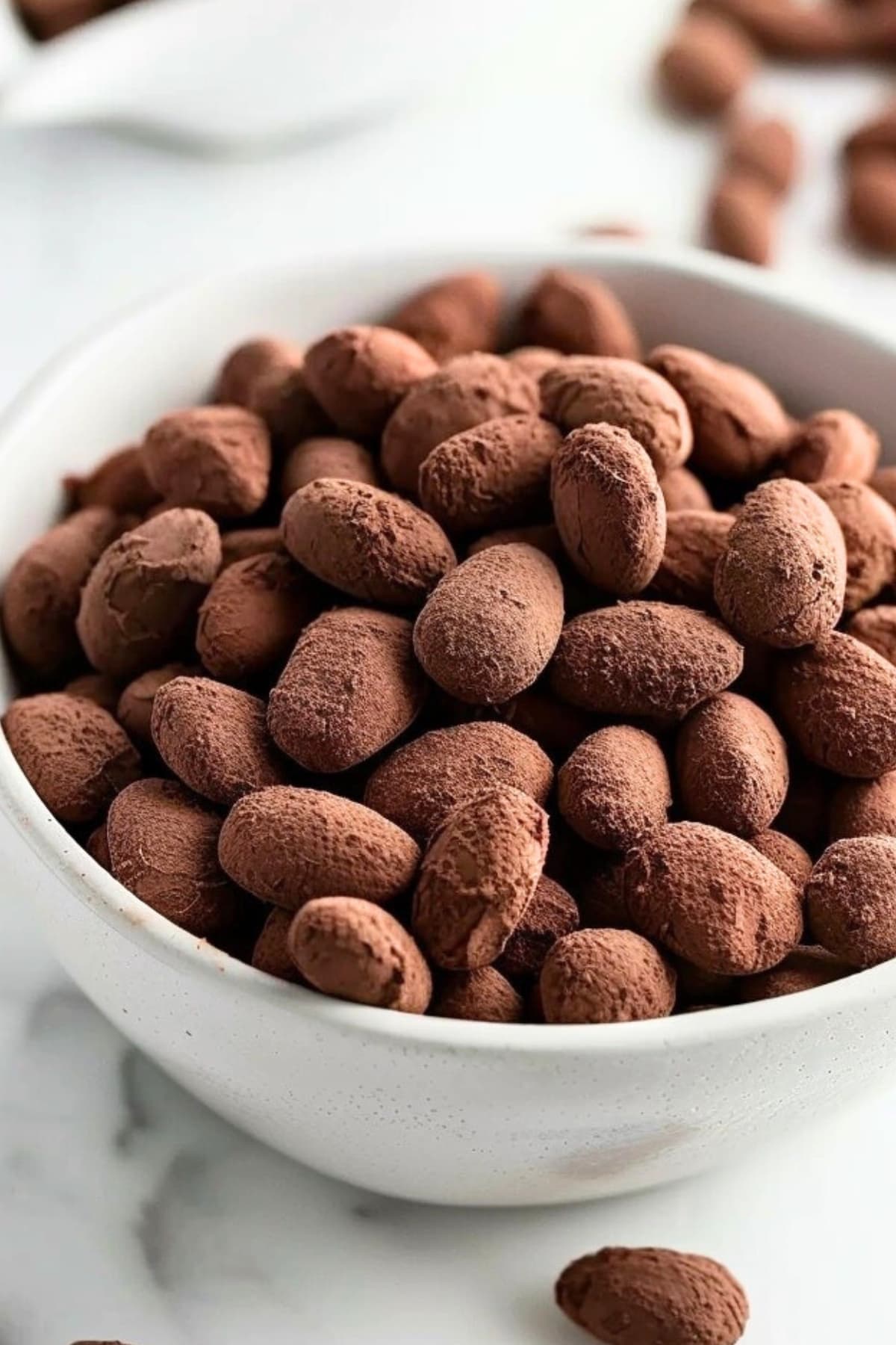 White bowl filled with chocolate and cocoa coated almonds.