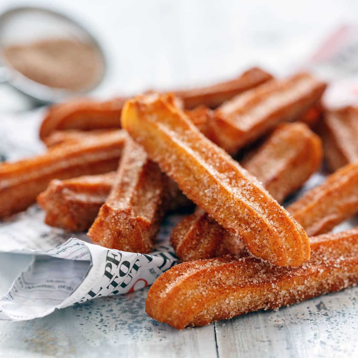 Bunch of churros coated with sugar cinnamon on newsprint parchment paper