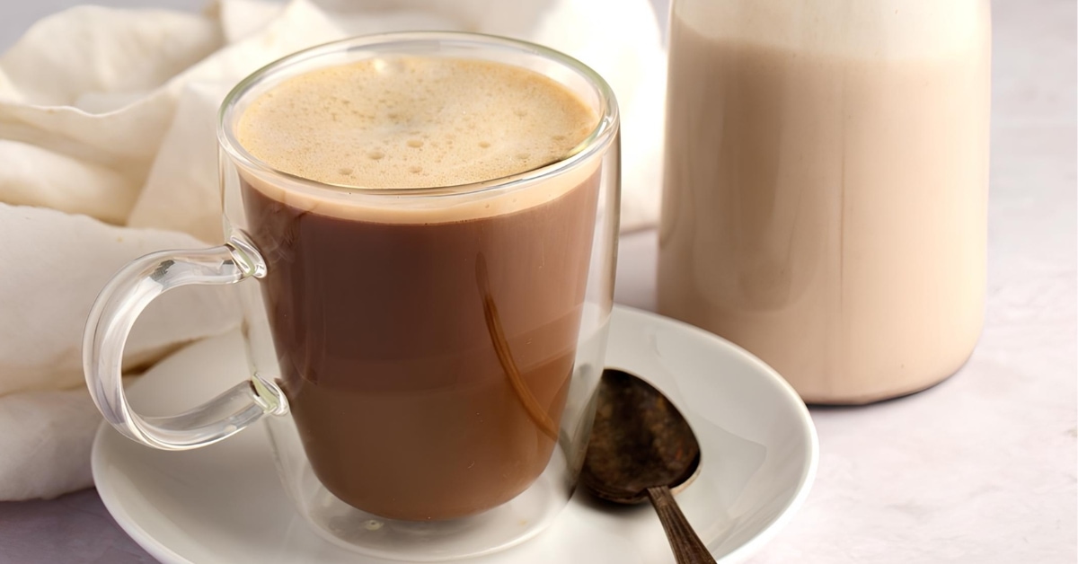 Foamy coffee on a glass mug beside a glass pitcher half filled with coconut creamer.