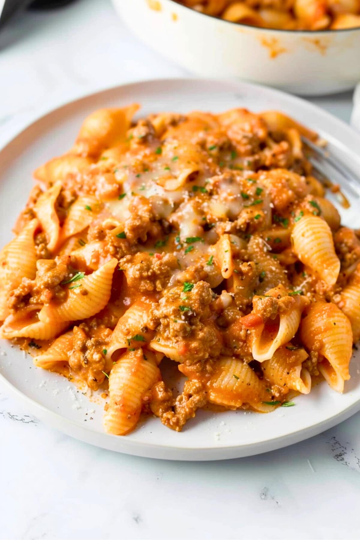 Beef and shells in cheesy tomato sauce served in a white plate.