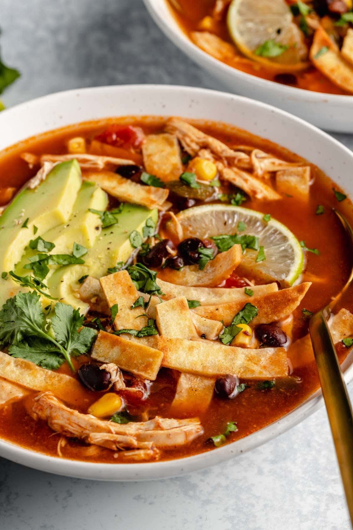 Bowl of homemade Crockpot Chicken Tortilla Soup garnished with sliced avocado,  lemon and cilantro
