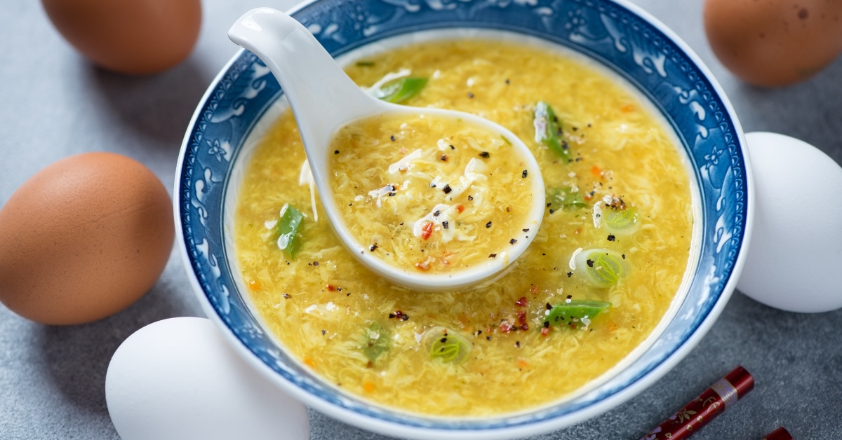 Egg drop soup on a blue Chinese bowl with chopped green onions.