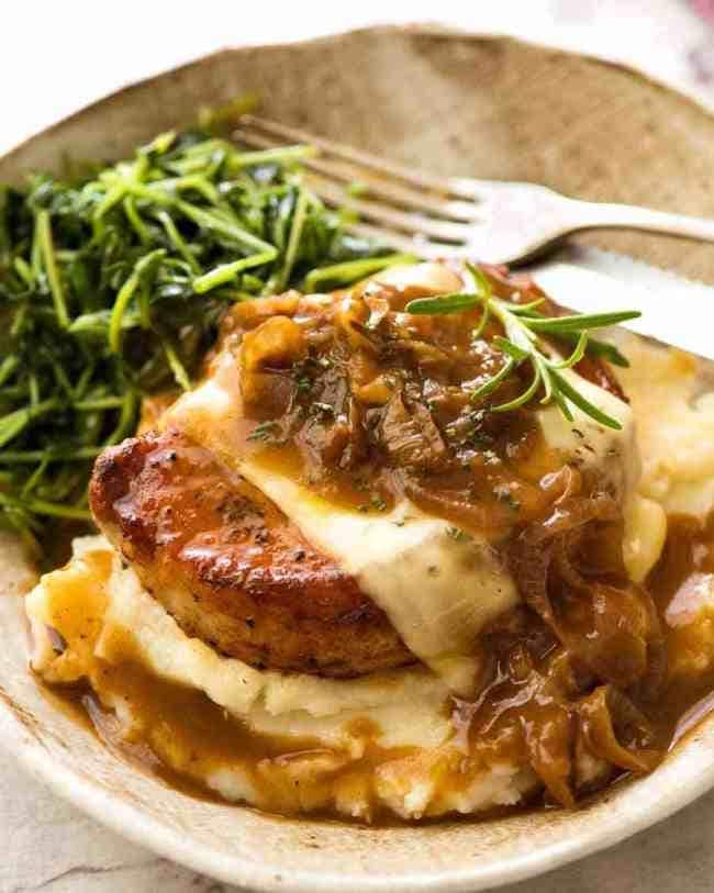 Pork chop on top of mash potatoes with melted cheese and French onion soup dripping on top. 