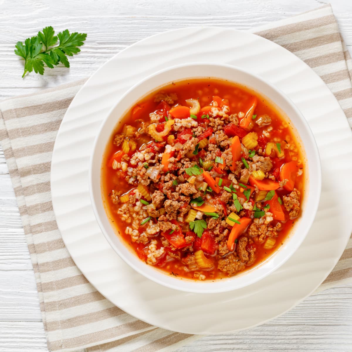 Top view of hamburger soup in a white bowl with veggies and meat. 