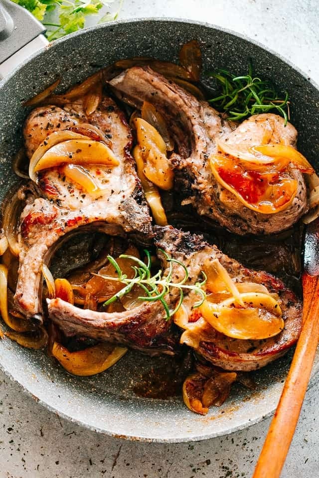 Porkchops cooked with apples and onions in a skillet. 