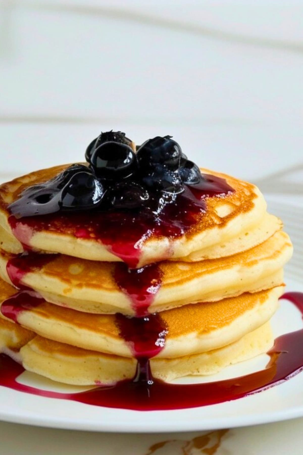 Thick fluffy pancakes topped with blueberry jam on a white plate.