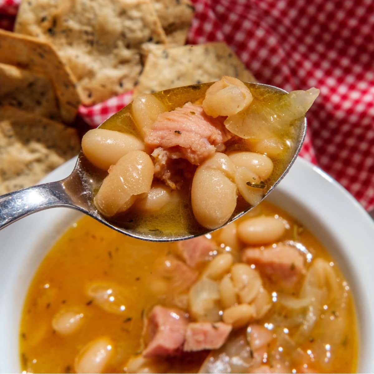 Spoon scooping beans and ham from the bowl.