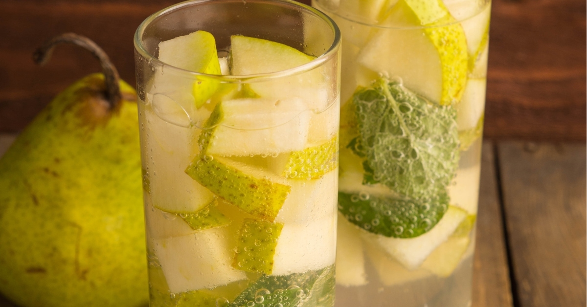 Two glasses of pear vodka cocktail on a wooden table garnished with sliced pear and mint.