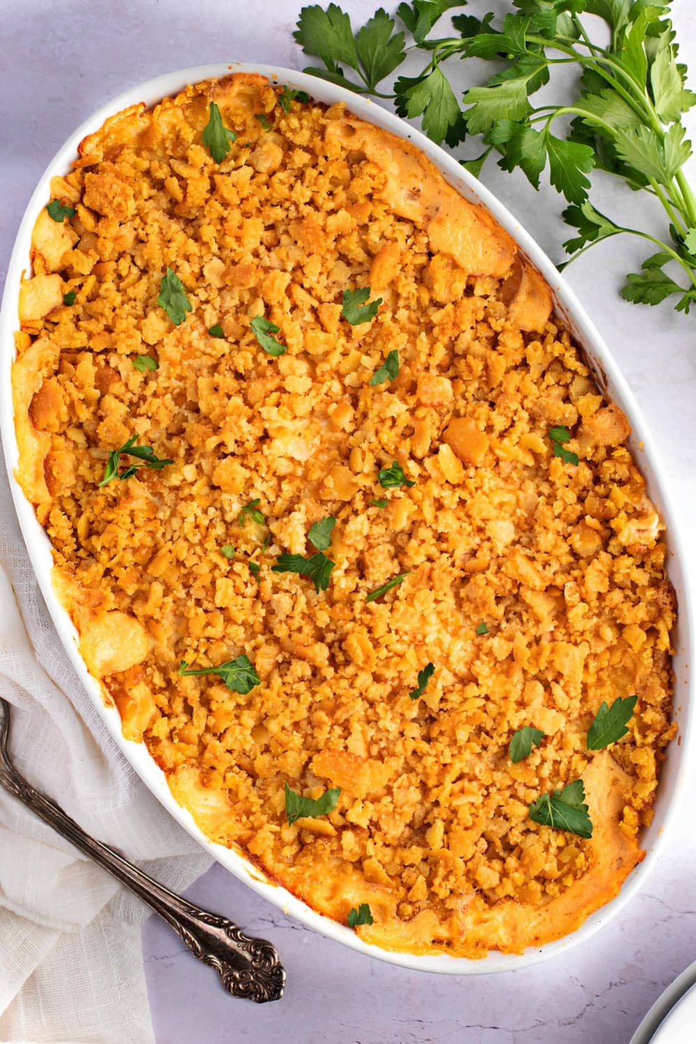 Million Dollar Chicken Casserole, Topped with Ritz Crackers and Melted Cheese. Sitting on a Marble Countertop with Linen and a Serving Spoon
